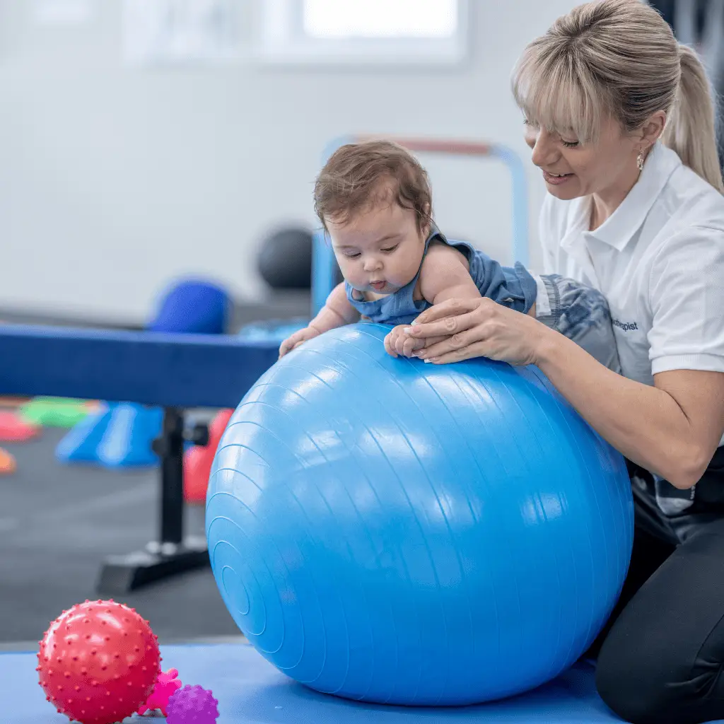 Infant doing Occupational Therapy with therapist using a large blue ball.